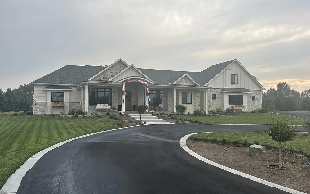 A completed custom home: stone and board and batten, a covered entry, a curved drive and new lawn